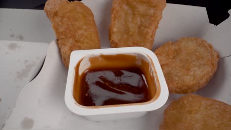 static macro view dipping chicken nugget in barbeque sauce, takeaway fast food, delivery, unhealthy