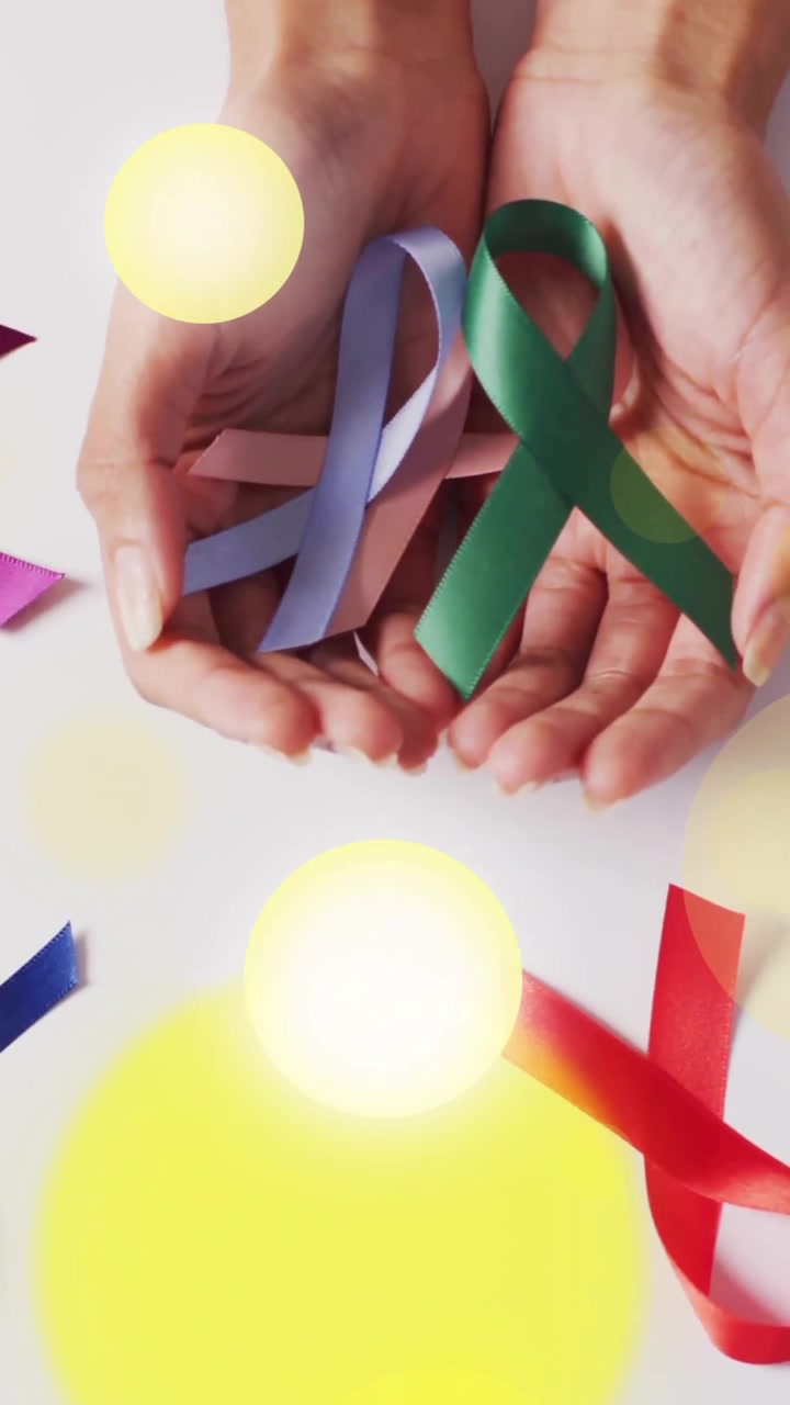 Mani che tengono nastri colorati per la consapevolezza, con sovrapposizione di punti luminosi giallo brillante.