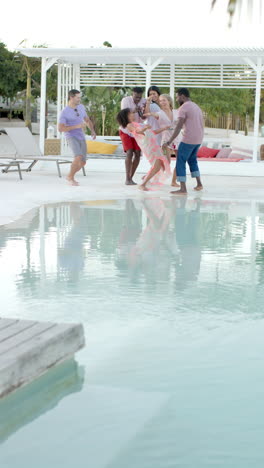 Vertical video of happy diverse group of friends dancing at pool