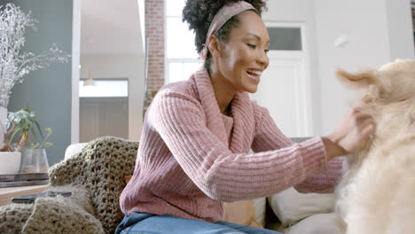 happy biracial woman petting golden retriever dog at home, slow motion