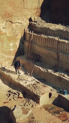 worker is drills stones with using pneumatic tool in the sand quarry. camera motion up. aerial view vertical video