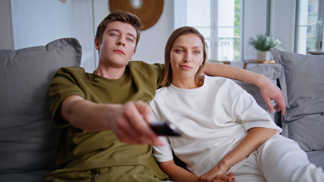 Family couple watching tv together at sofa closeup. Boyfriend switching channels