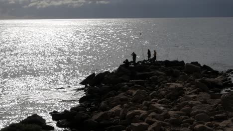 fishermen on rocky coastline of cabo de huertas, alicante, with sunlight reflecting