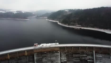 aerial shot of a lake created by the arch dam vir in czech republic with dense pine forest covered by snow on all sides on a cloudy wintry evening