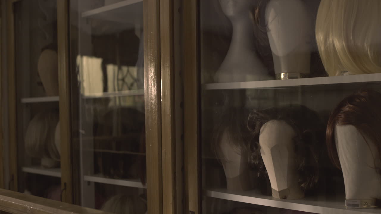 Camera pans across women's wigs in a wooden box, showcasing many retro 1950s hairstyles