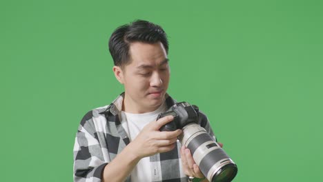 close up of asian photographer looking at the pictures in the camera then screaming goal celebrating satisfied with the result while standing on green screen background in the studio