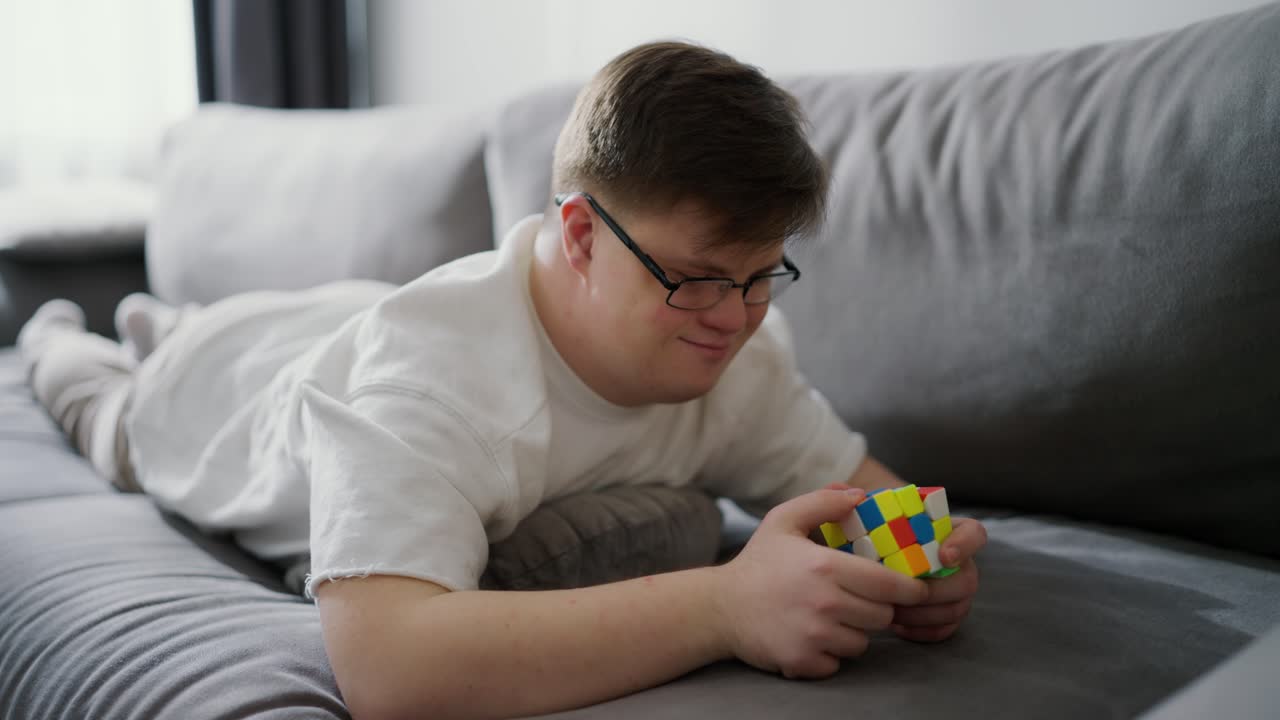 hombre con síndrome de down descansando en el sofá en casa y jugando con el cubo de rubik