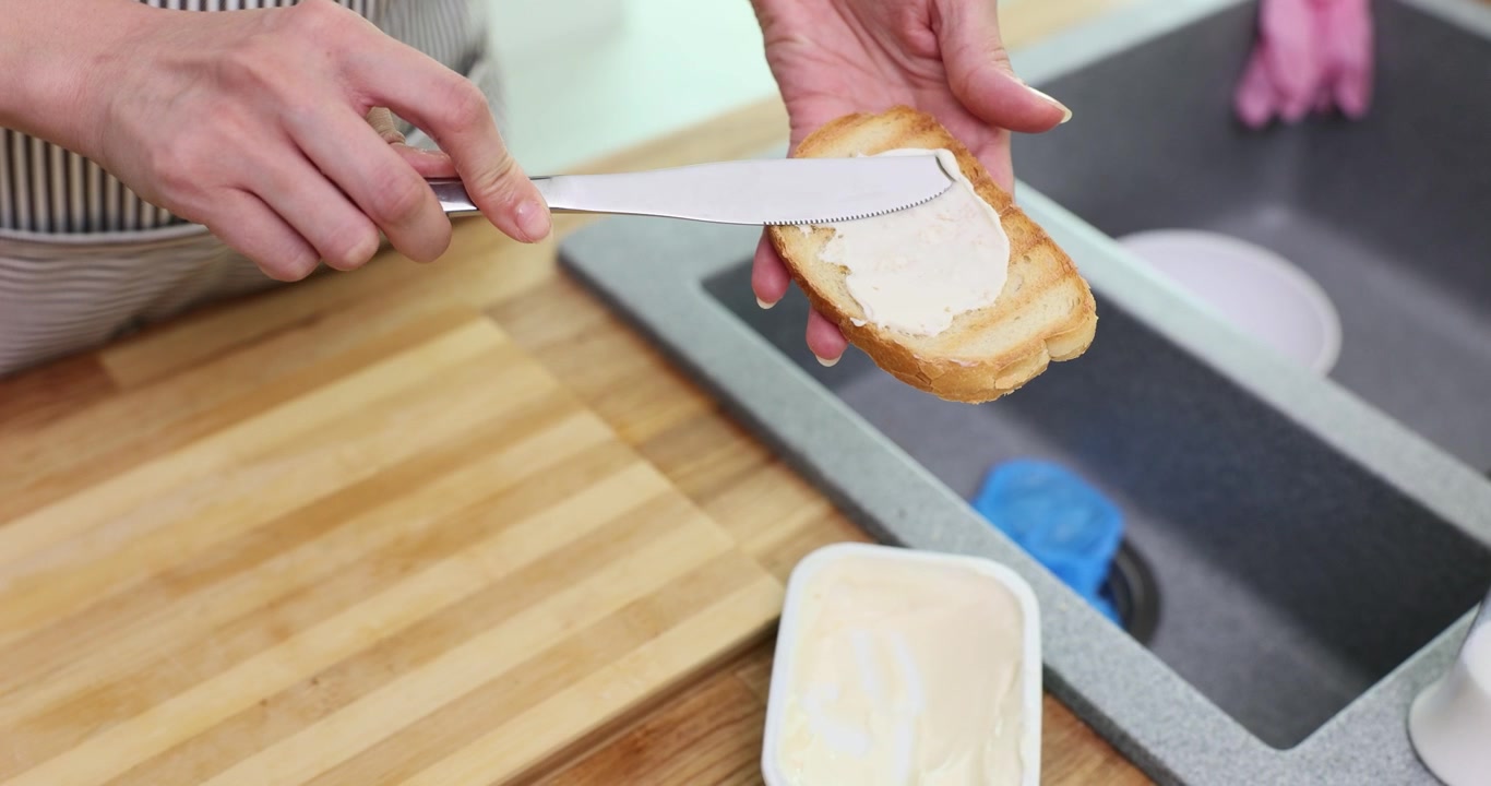 Woman in apron spreads soft cheese on toasted bread slices