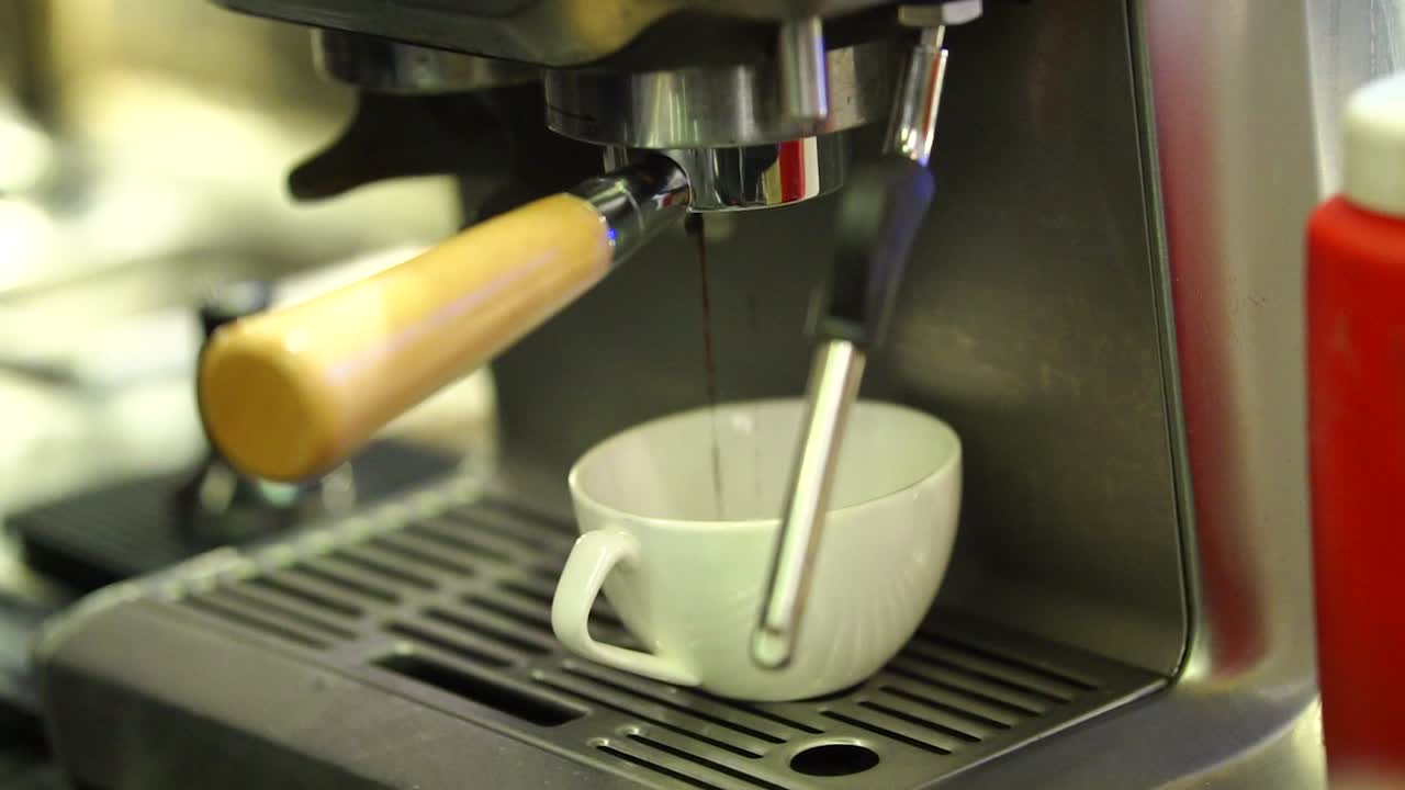 café recién hecho goteando en una taza blanca debajo de la máquina expreso
