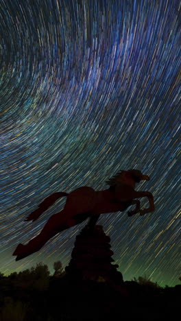 vertical timelapse of star trails swirling in the night sky over the silhouette of a horse sculpture at the wild horses monument, creating a mesmerizing celestial effect.