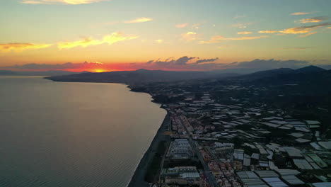 Eine-Sanfte-Luftaufnahme-Eines-Farbenfrohen-Sonnenuntergangs-In-Einer-Stadt-An-Einer-Ruhigen-Küste-In-Spanien