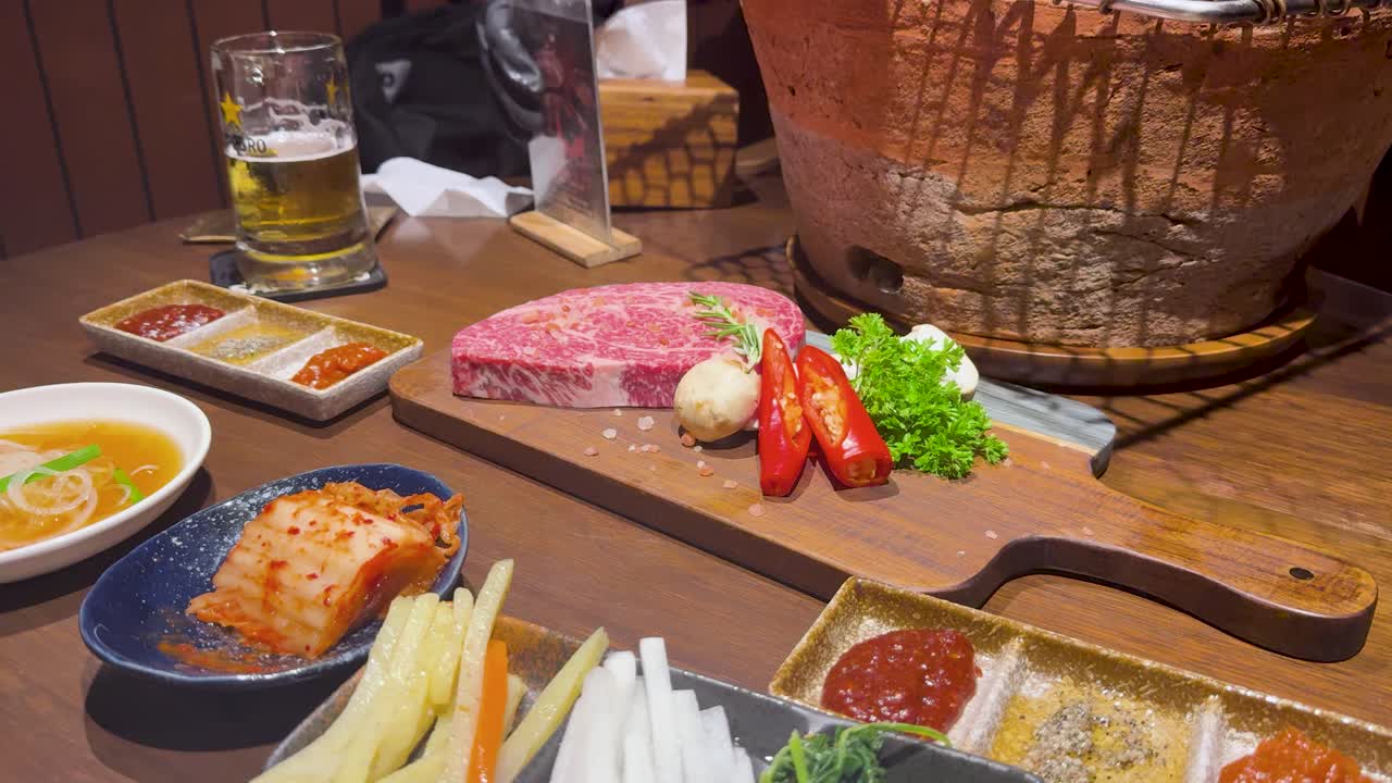 レストランのテーブルに置かれた生の和牛と伝統的なおかずをハイアングルから捉えた静止画
