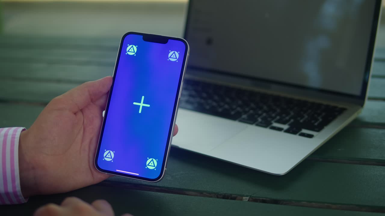Woman hand holding phone with chroma key screen in front of laptop outdoor. Smartphone with green screen close-up