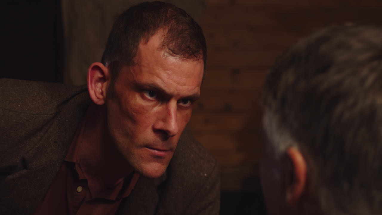 An angry man shouts to another man and eases down when he gets an answer during an interrogation