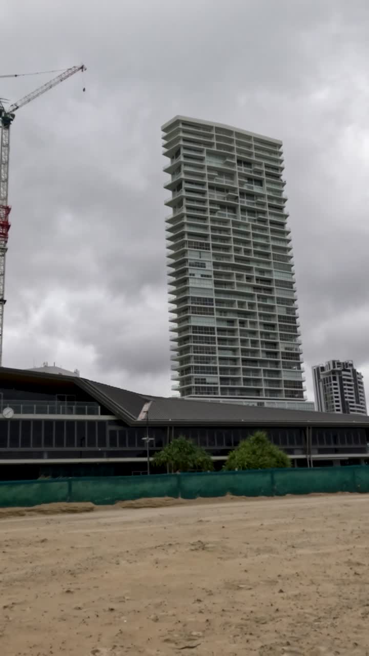 una escena de playa tormentosa con fuertes vientos y olas turbulentas del océano bajo cielos nublados, mostrando edificios urbanos en el fondo