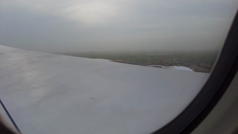 through aircraft window view of airplane flying through beautiful clouds and landing on green landscape