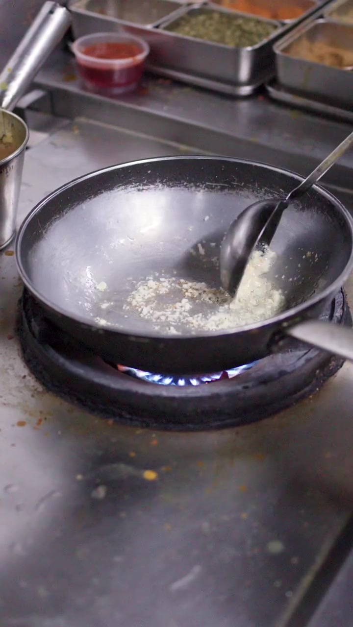 Close-up shot of a chef stirring ingredients in a wok on a commercial gas stove.