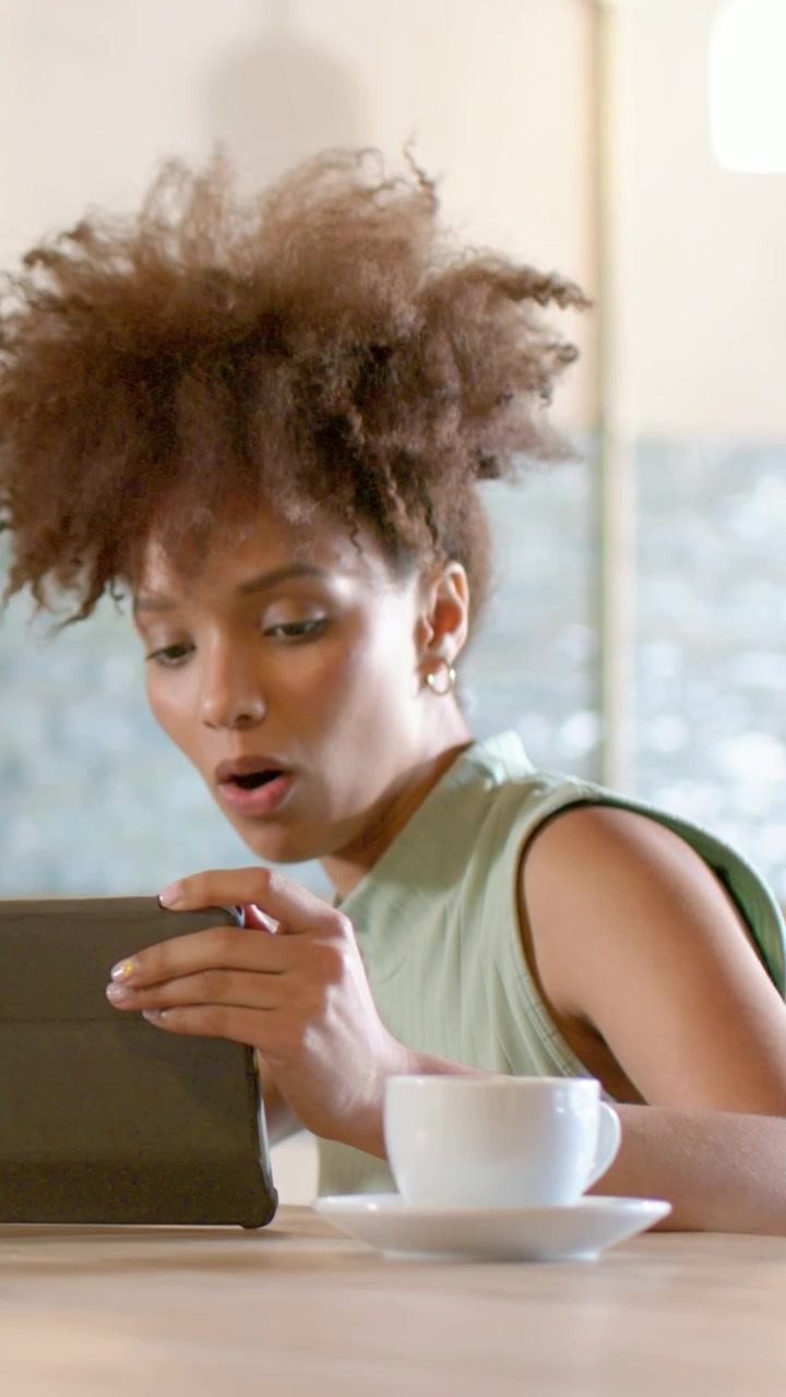 Vertical video: Noticing tablet, woman in pale top adjusting grip, tapping, viewing content at cafe