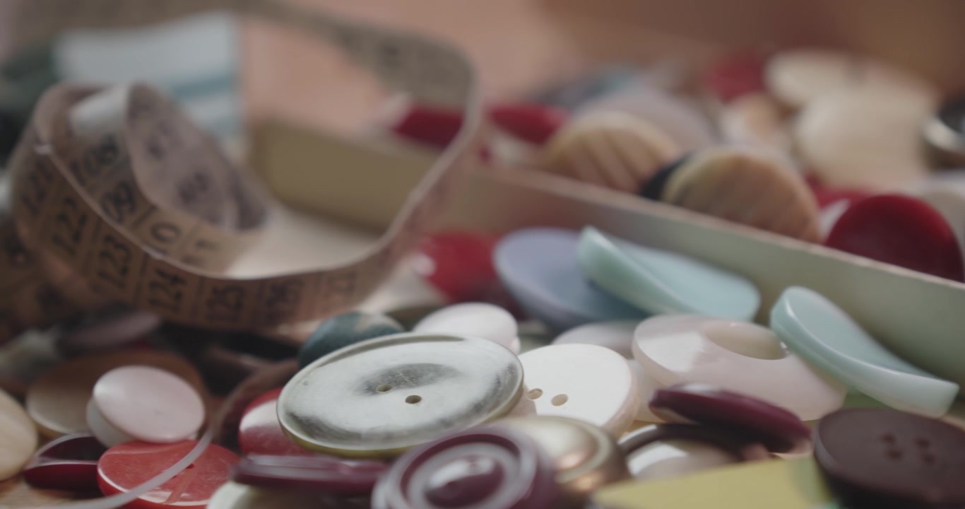 Slow pan across a tailor's button collection with a measuring tape, showcasing sewing supplies, garment making and textile craftsmanship in macro detail.