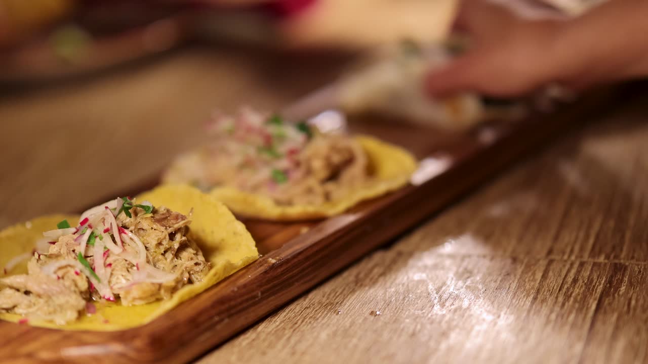 Hands arrange tacos on a wooden board in a warmly lit restaurant environment