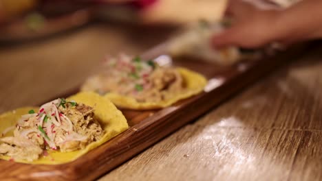 hands arrange tacos on a wooden board in a warmly lit restaurant environment