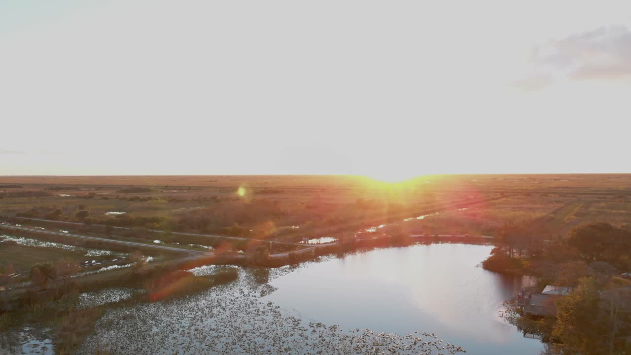 A wide aerial dolly forward over a Florida nature preserve, revealing sunlit wetlands and a reflective pond at golden hour