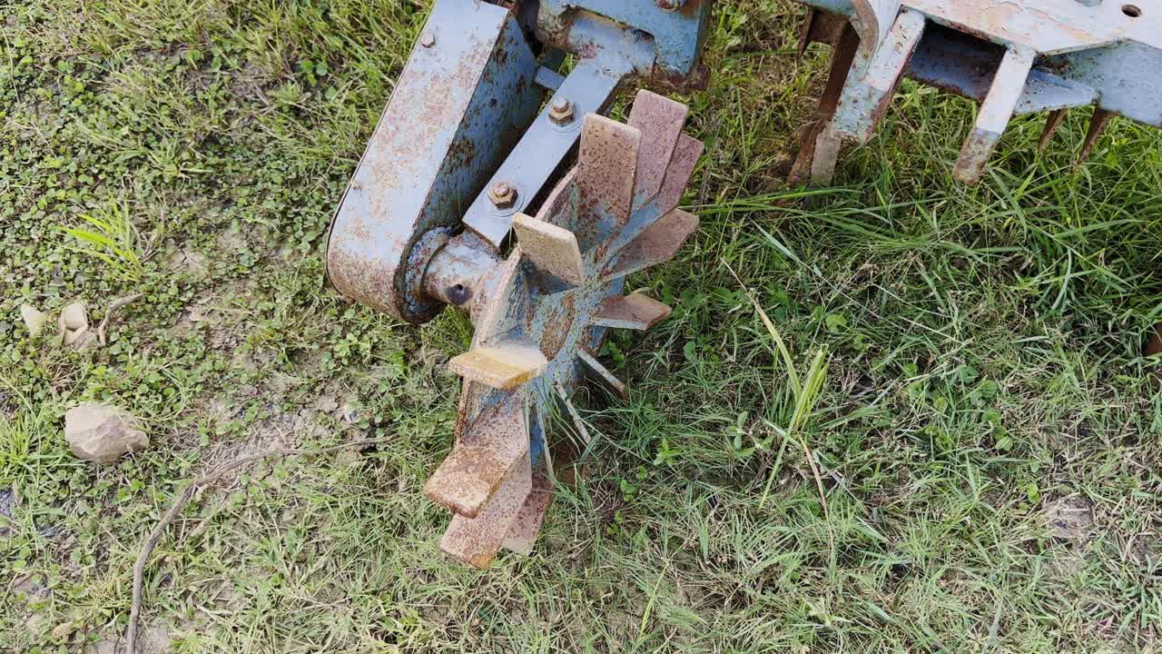 Camera circling around old rusty farming equipment lying on grassy ground, showcasing textures of age, metal decay, and rural life in detail