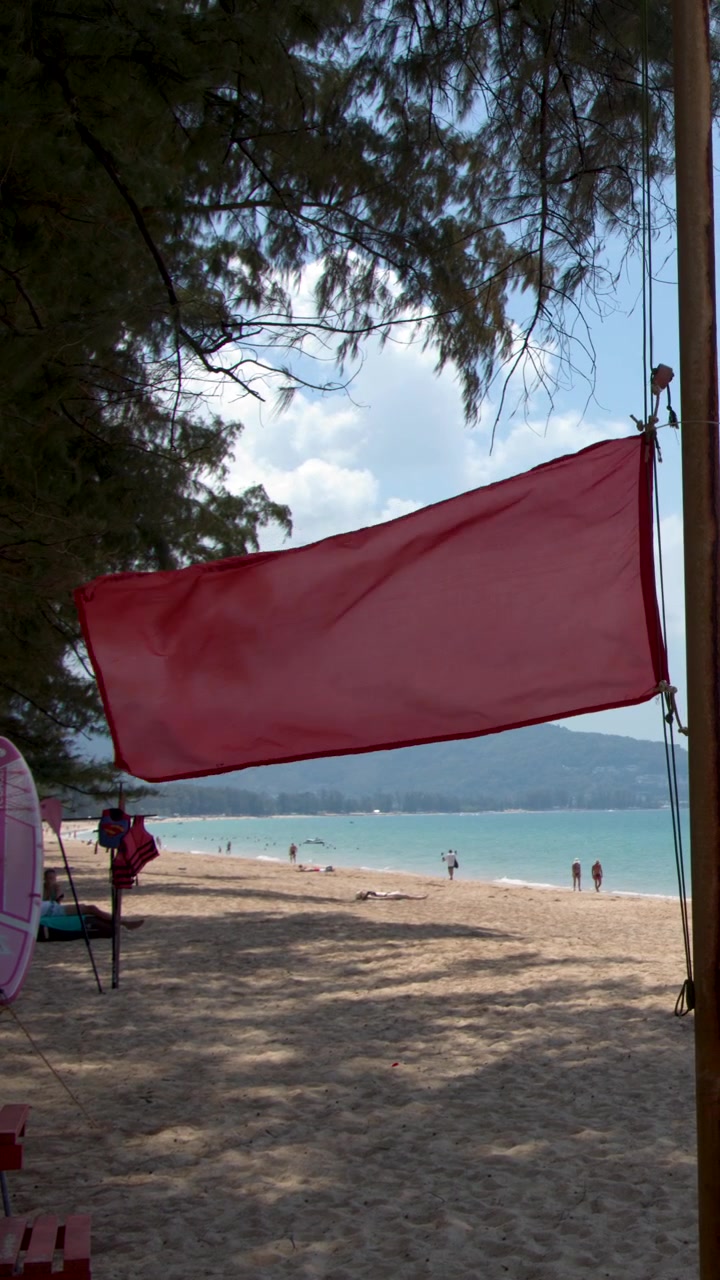 Una bandiera rossa di avvertimento del bagnino sventola su una spiaggia tropicale soleggiata a Phuket, Thailandia