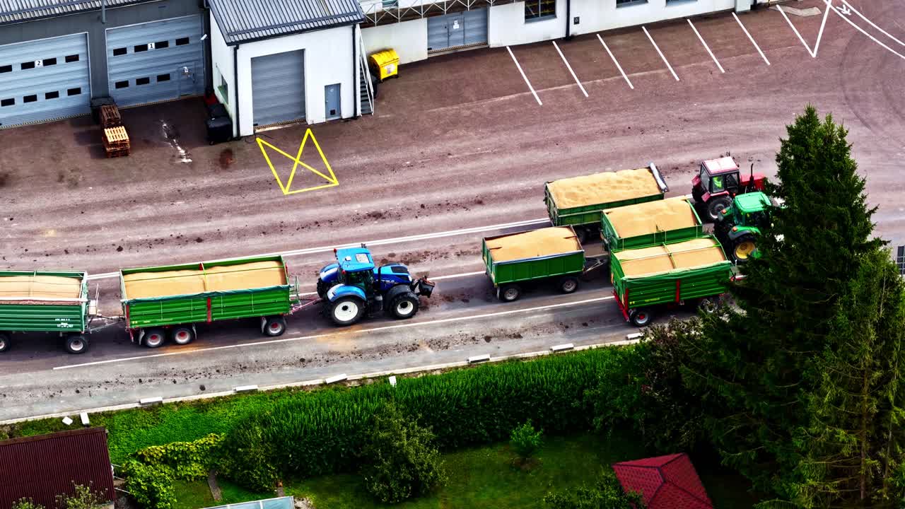 Aerial footage of tractors with the grain harvest waiting to be unloaded at a warehouse