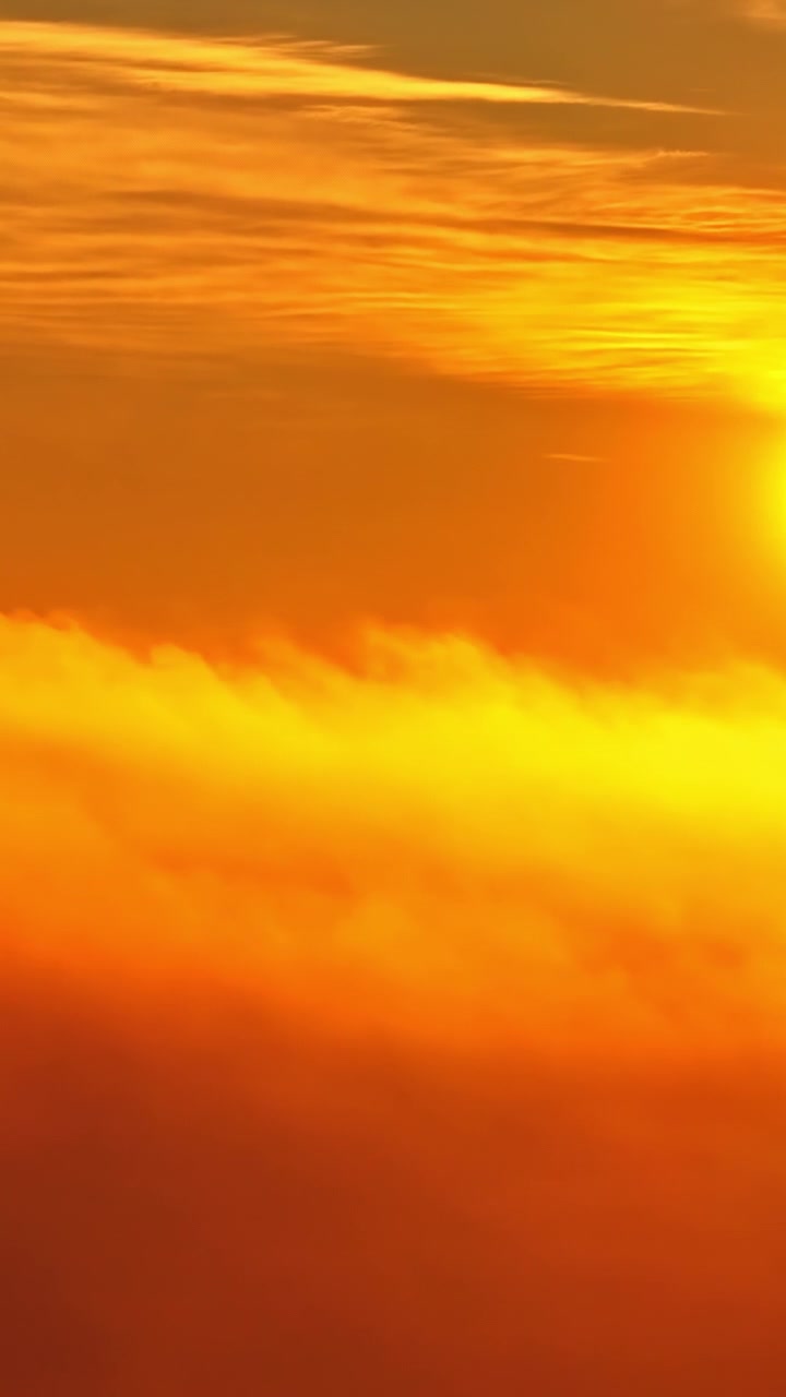 Vista aerea verticale di un tramonto dorato e nuvole arancioni ad alta quota con il bagliore del sole e una luce calda e drammatica in un cielo bellissimo durante il crepuscolo serale.