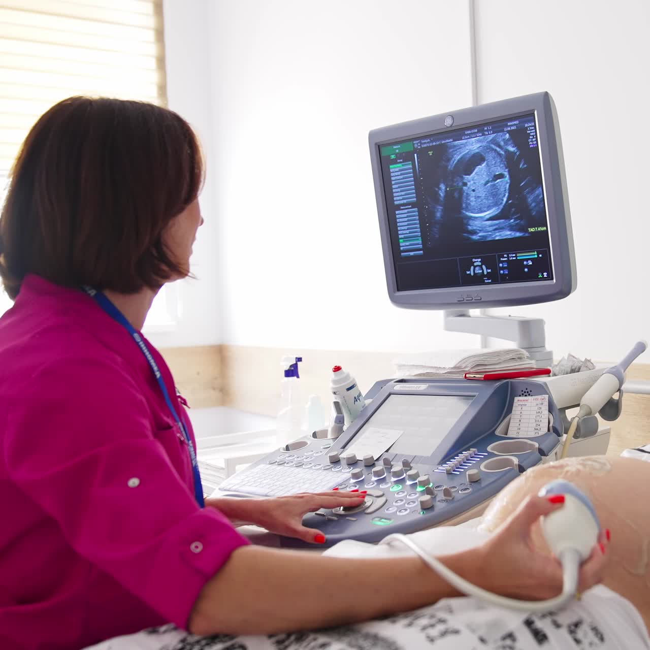 Future mother at the ultrasound examination. Female doctor sits at ultrasonic apparatus, looking at the screen and commenting the picture