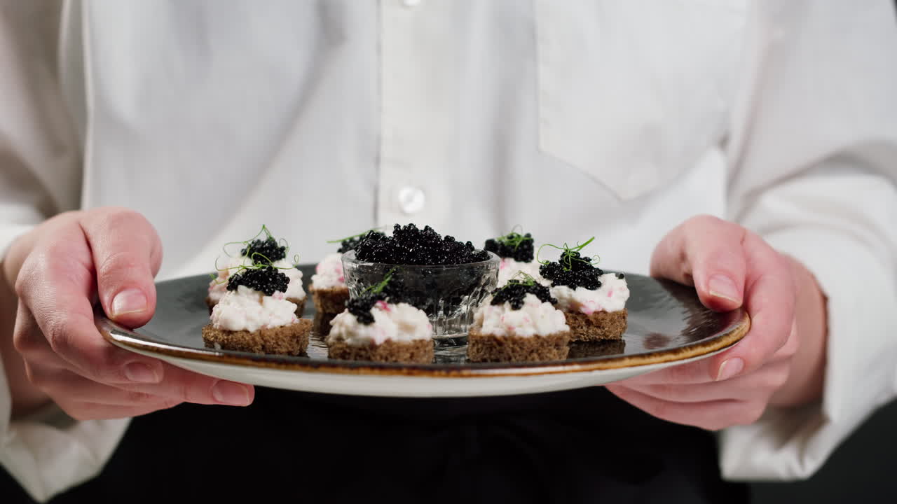 Chef presenteert een bord met gastronomische canapés met zwarte kaviaar