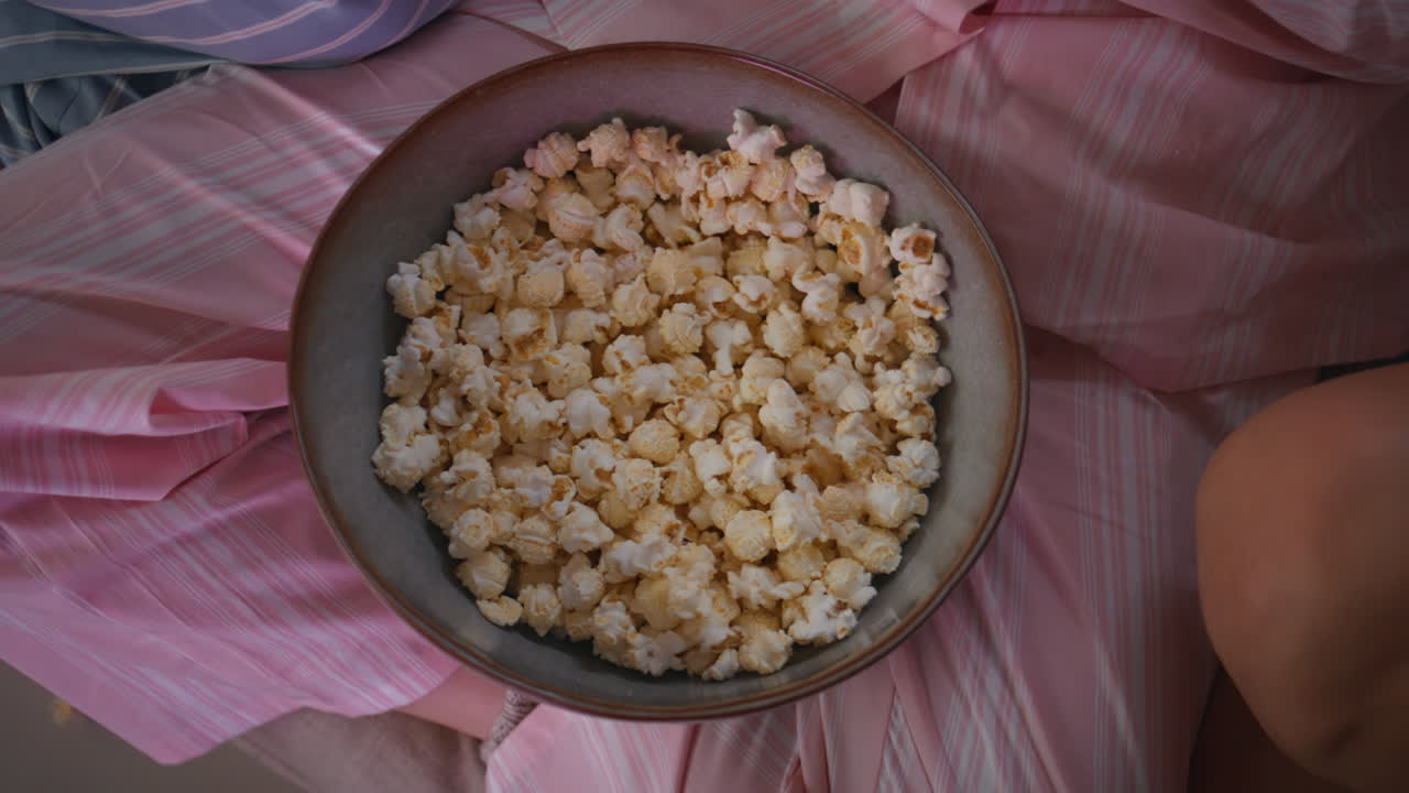 Primo piano di una ciotola di popcorn deliziosi. Mani femminili irriconoscibili prendono un antipasto