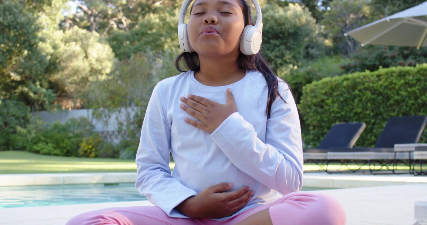 Teen girl breathing by pool following audio on headphones placing hands on chest bottle right
