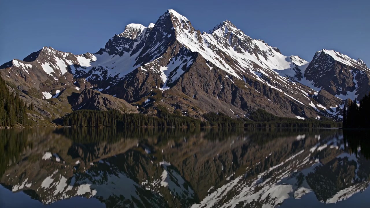 Cime montuose innevate riflesse nell'acqua calma del lago