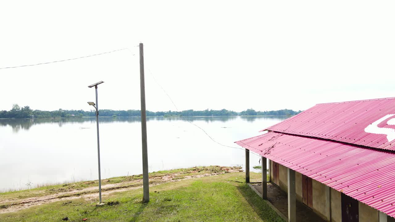 An Electric Pole Stands Beside a Rural House Surrounded by Floodwaters in the Haor Area of Sylhet, Bangladesh, South Asia - Pan Down Shot