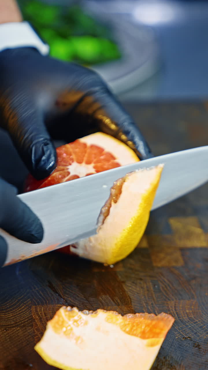 Unrecognized cook wearing black latex gloves peeling off grapefruit carefully. Juice from a fruit pours on the wooden blackboard. Close up. Vertical video.