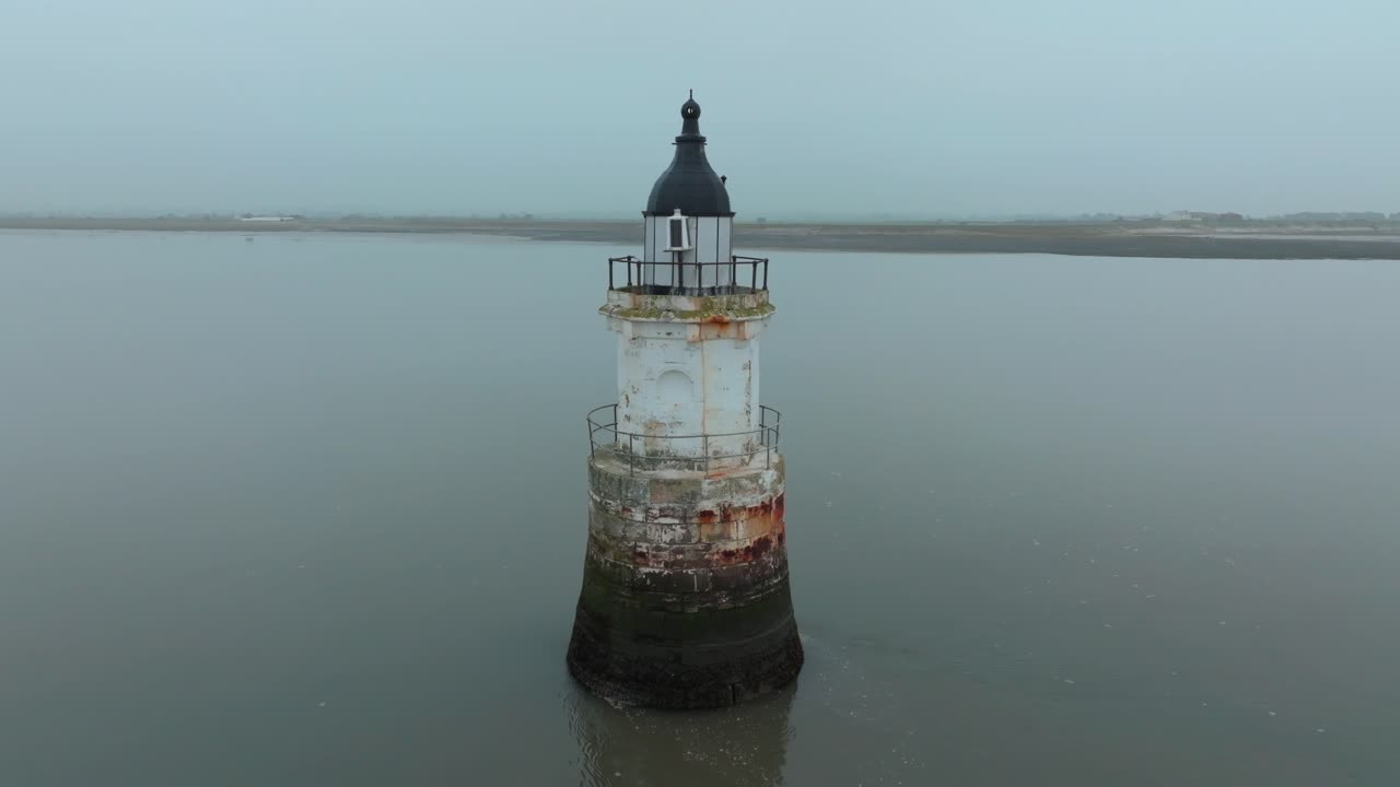 Old Rusted Derelict Lighthouse In Calm Water With Misty Coastline And Flashing Light on Tower. Camera Slow Orbit. Plover Scar Lighthouse, Lancashire, UK