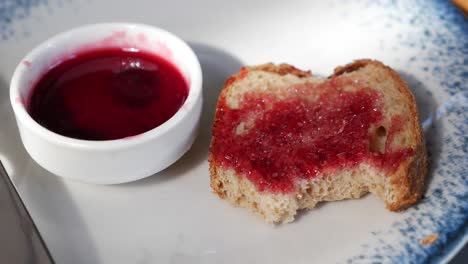 primer plano de una rebanada de pan tostado con mermelada roja en un plato blanco