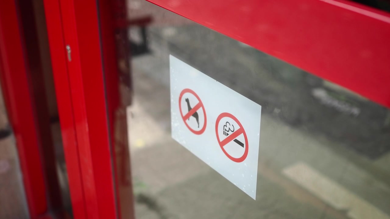 Close-up of No Smoking and No Dogs Signs on a Red Glass Door