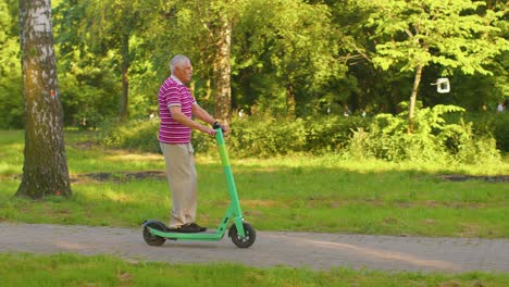 Caucasian-old-gray-haired-senior-stylish-man-grandfather-riding-electric-scooter-in-summer-park