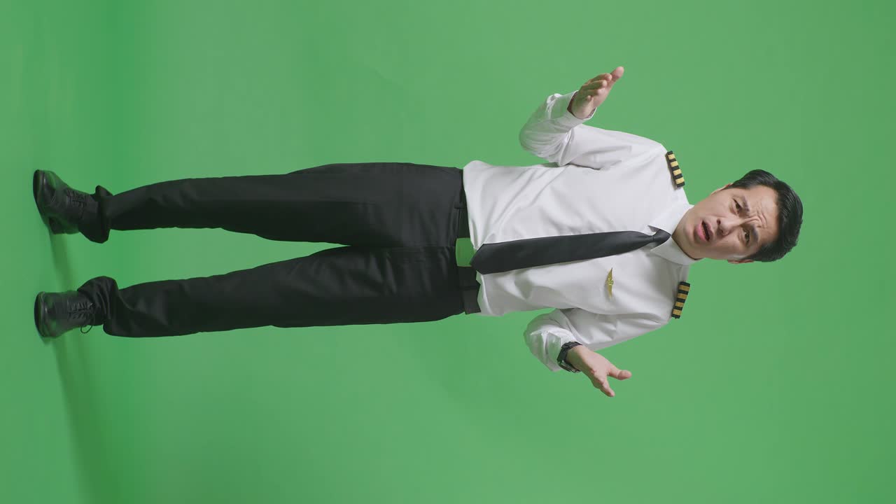 "아시안 남성 조종사가 ""왜""라고 묻고, 녹색 스크린 배경 스튜디오에서 의심스럽게 서 있습니다."