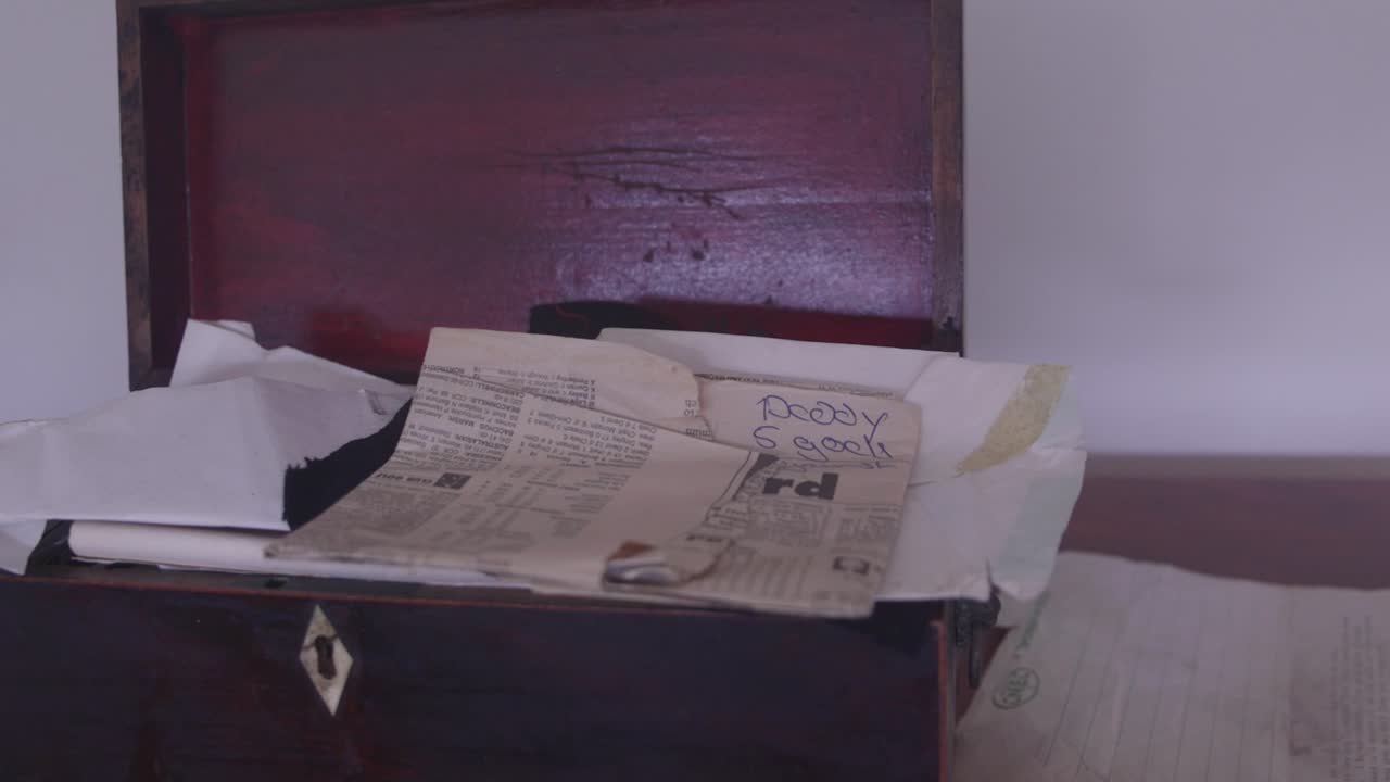 Una mano chiude un'antica scatola di legno piena di carte e lettere d'epoca, evocando nostalgia e storia. Perfetta per documentari storici o film d'epoca