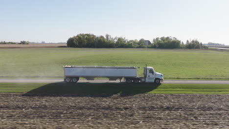 semi truck pulling a hopper trailer driving on rural countryside road, transporting harvested crop, aerial