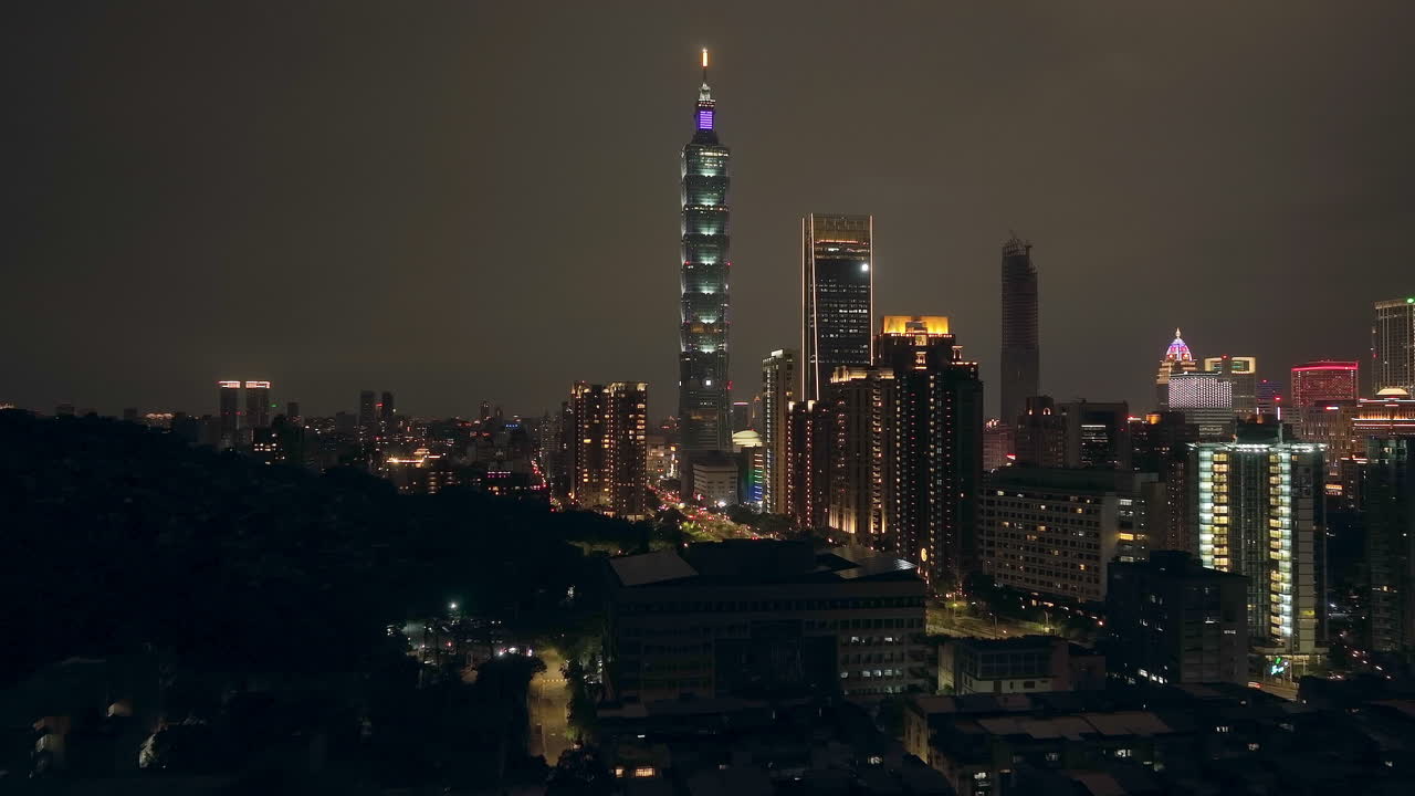 Aerial forward shot showing cityscape skyline of taipei city at night - along palm trees and skyscraper 101 tower