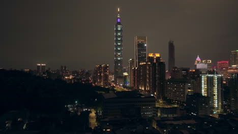 aerial forward shot showing cityscape skyline of taipei city at night - along palm trees and skyscraper 101 tower