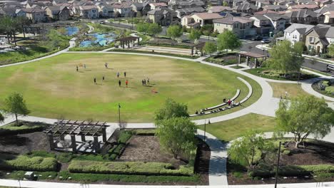 Aerial,-reverse,-drone-shot-tilting-away-from-kids-playing-soccer,-on-a-grass-field,-sunny-day,-in-a-neighborhood,-in-Los-Angeles,-California