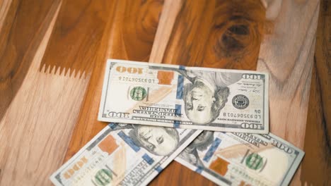 One-hundred-dollar-bills-slowly-falling-on-a-wooden-table-in-slow-motion-top-down-view