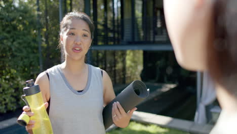 happy asian female friends with exercise mat and water bottle discussing on terrace, slow motion