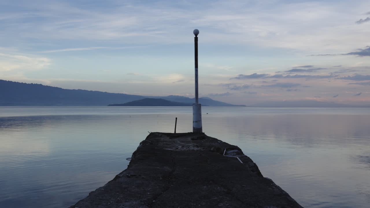바다 벽은 항구 가장자리에서 어나오고 구름은 천천히 흐릿한 파스텔 파란 하늘을 가로질러 움직입니다.